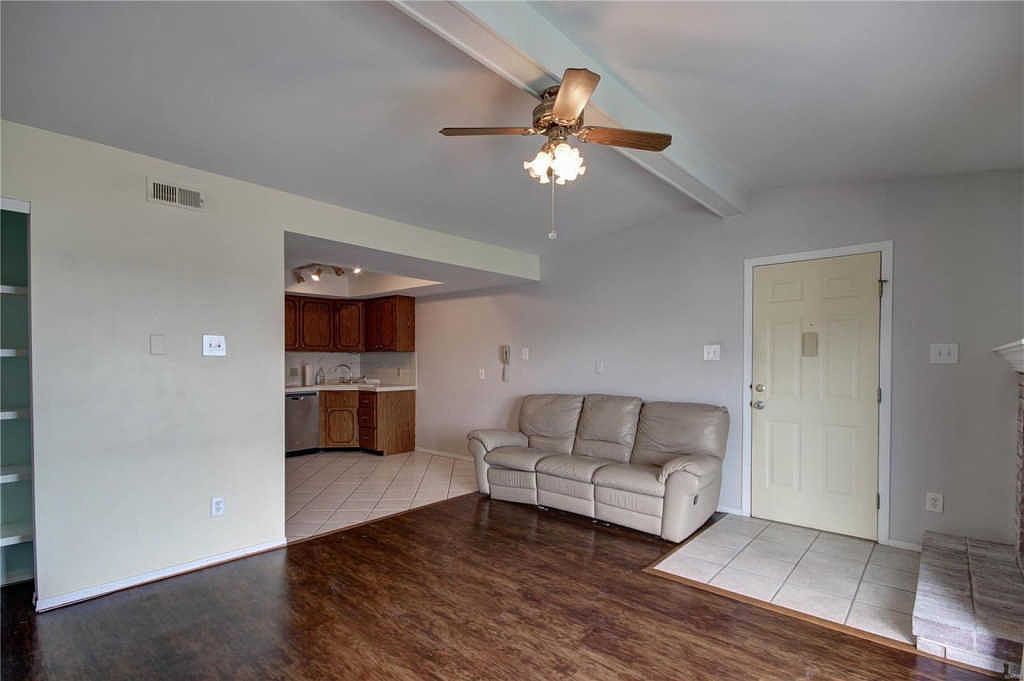 Living room with vaulted beamed ceiling, ceiling fan and front entry; kitchen beyond